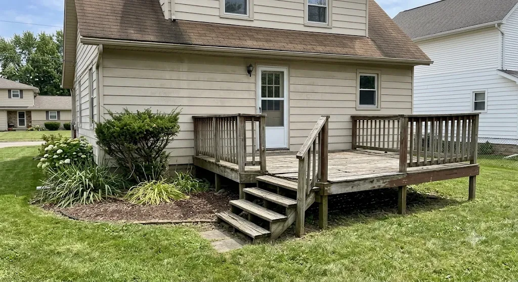 Weathered gray wood deck with worn railing behind a Northeast Ohio home